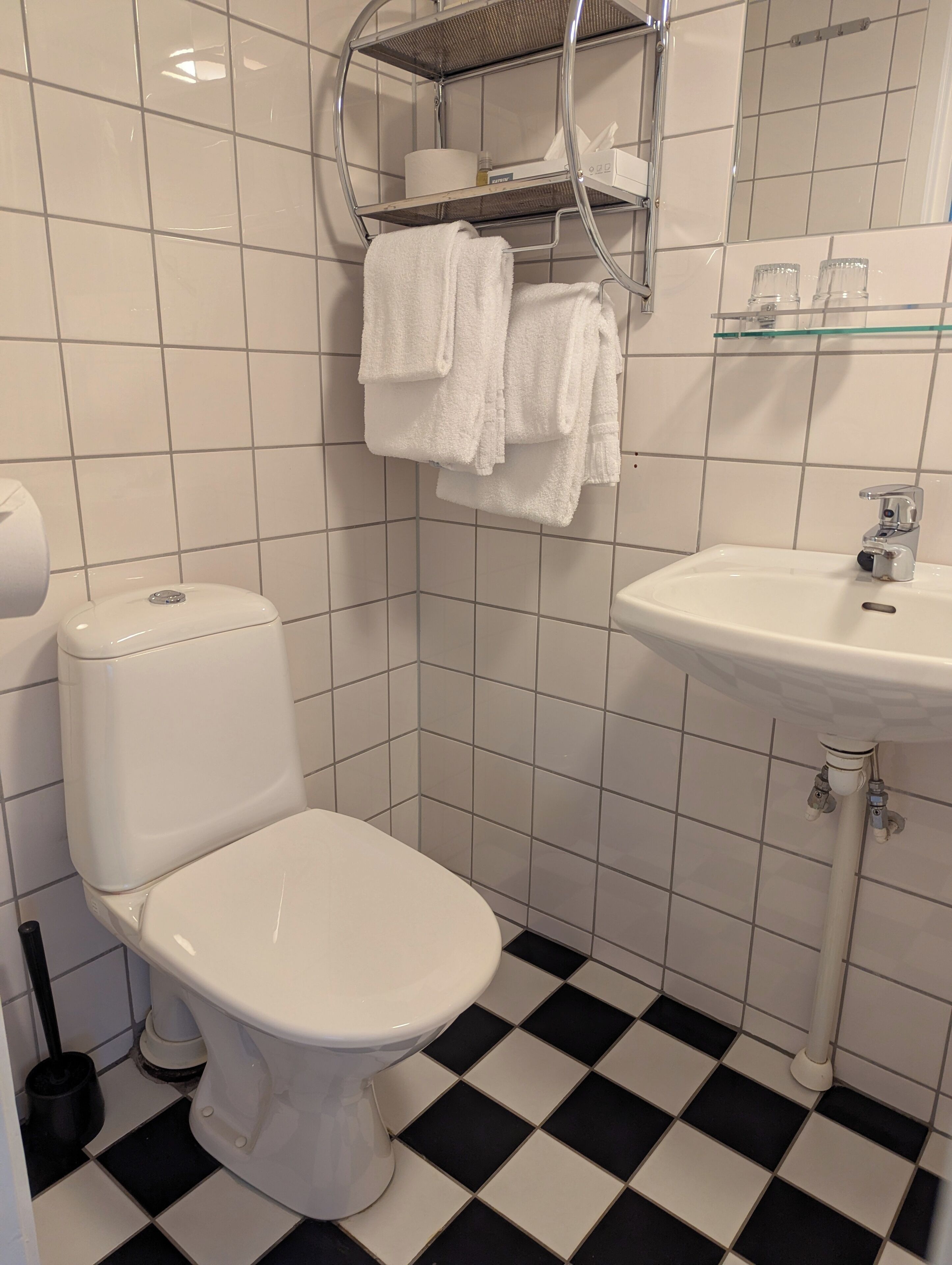 A bathroom with a toilet, a sink, and a shelf with towels.