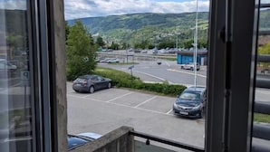 A view from a window overlooking a parking lot with cars, a blue building, and a hilly landscape.