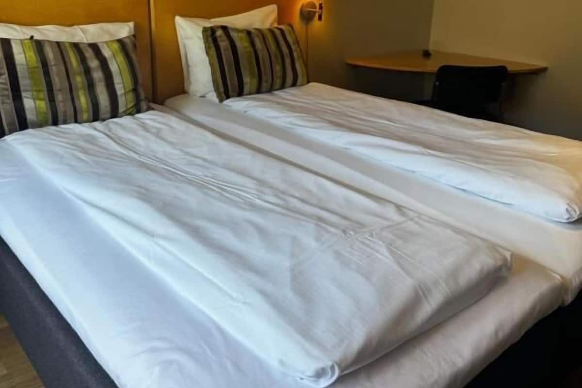 Habitación de hotel con una cama grande, dos almohadas, una mesita de noche y una lámpara.