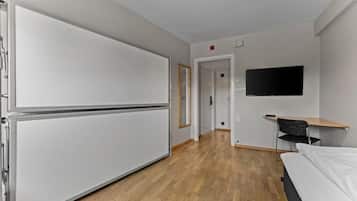 A hotel room with a bed, a desk, a chair, a television, and a door leading to another room.