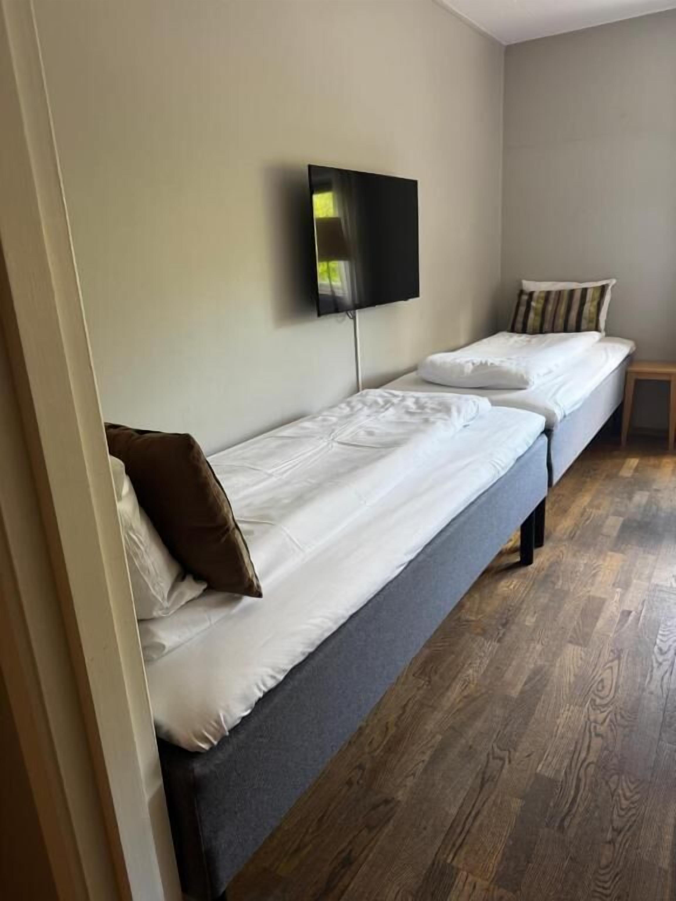 A room with two single beds, a television mounted on the wall, and a small wooden table.