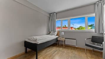 Camera da letto con un letto singolo, un comodino con una lampada, una sedia e una finestra con tende.