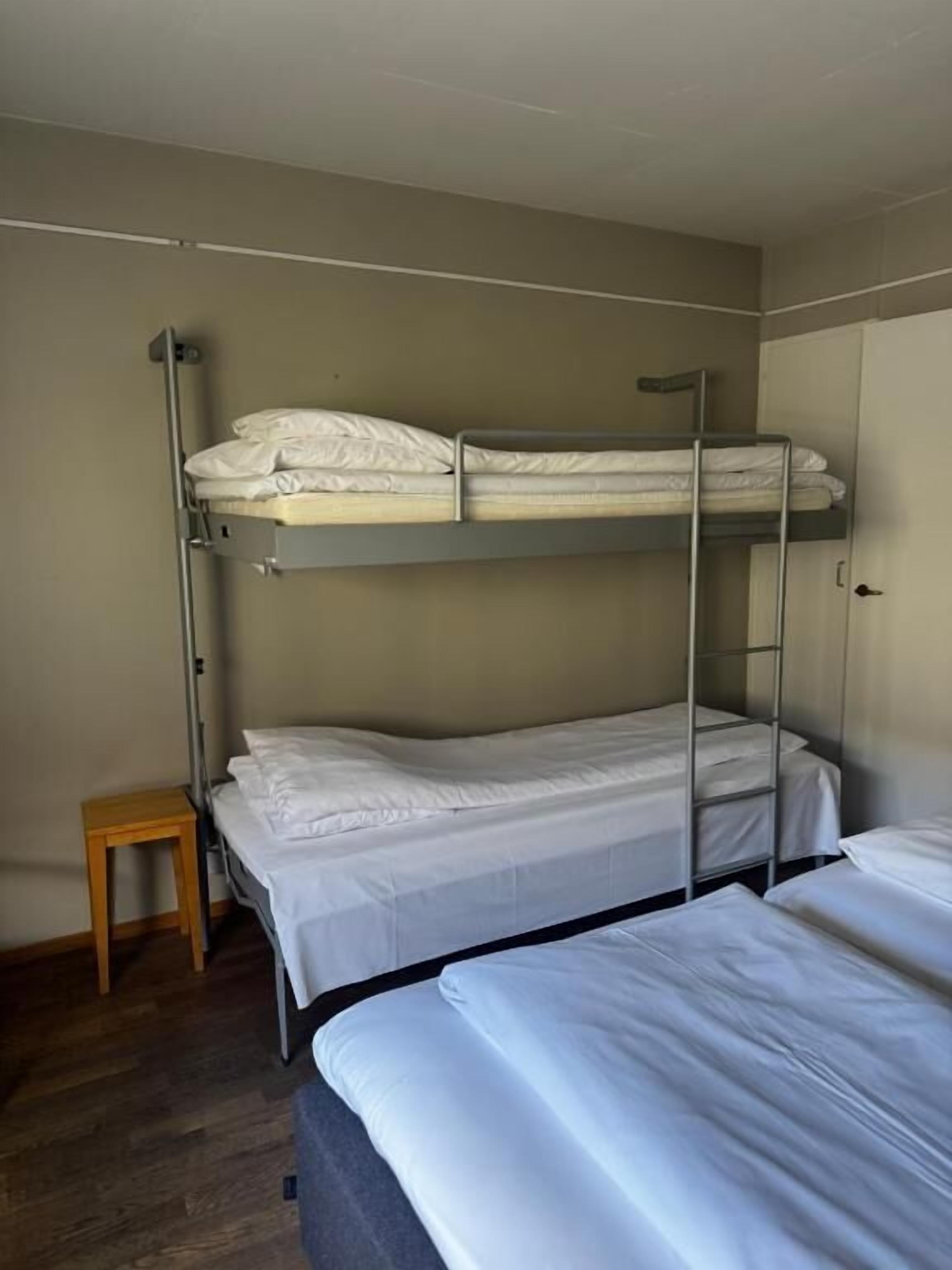 A bunk bed room with a small wooden stool and a wardrobe.