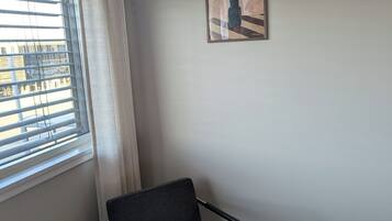 A room with a single chair, a bed, a window with blinds, and a painting on the wall.