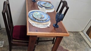 Une table de salle à manger en bois, sur laquelle sont posées deux assiettes bleues et un verre assorti. L’ensemble est placé sur un sol carrelé de carreaux hexagonaux.
