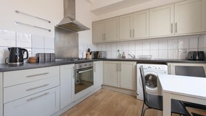 A modern kitchen with white cabinets, a stainless steel range hood, a built-in oven, a washing machine, and a dining area with a table and chairs. - Split-level spacious family apartment (London)
