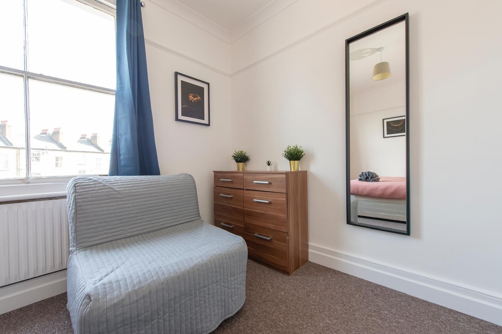 Un dormitorio con una cama, un aparador, una ventana que ofrece vistas a edificios y dos cuadros en la pared.