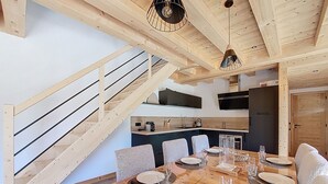 Eine moderne Küche mit dunklen Schränken, einer Holztreppe und einem Essbereich mit einem für vier Personen gedecktem Holztisch.