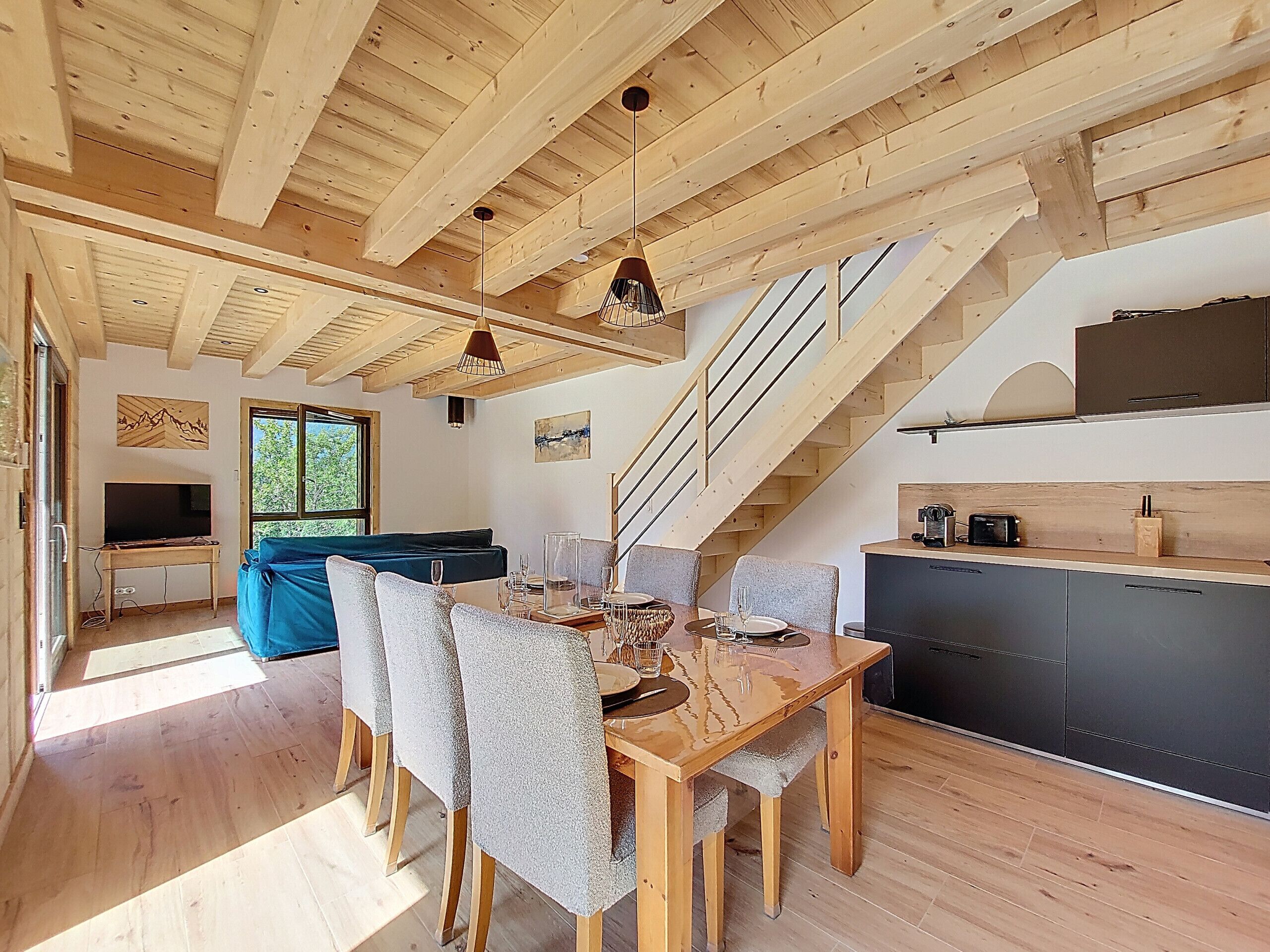A modern interior with a wooden ceiling, a dining area with a table and chairs, a kitchen area, and a staircase.