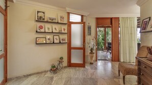 Un couloir avec une porte en bois, des œuvres d’art encadrées accrochées aux murs, un banc en osier et une plante en pot.