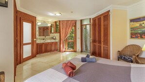 Une chambre avec un lit, une chaise, une salle de bain avec un miroir et une vue sur la verdure.