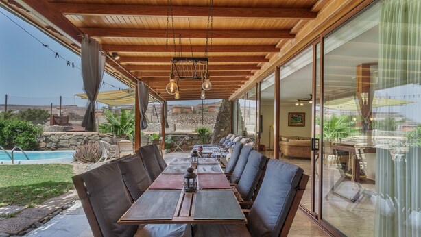 Un espace de restauration en plein air doté d’un plafond en bois, de grandes fenêtres et offrant une vue sur une piscine et un paysage verdoyant.