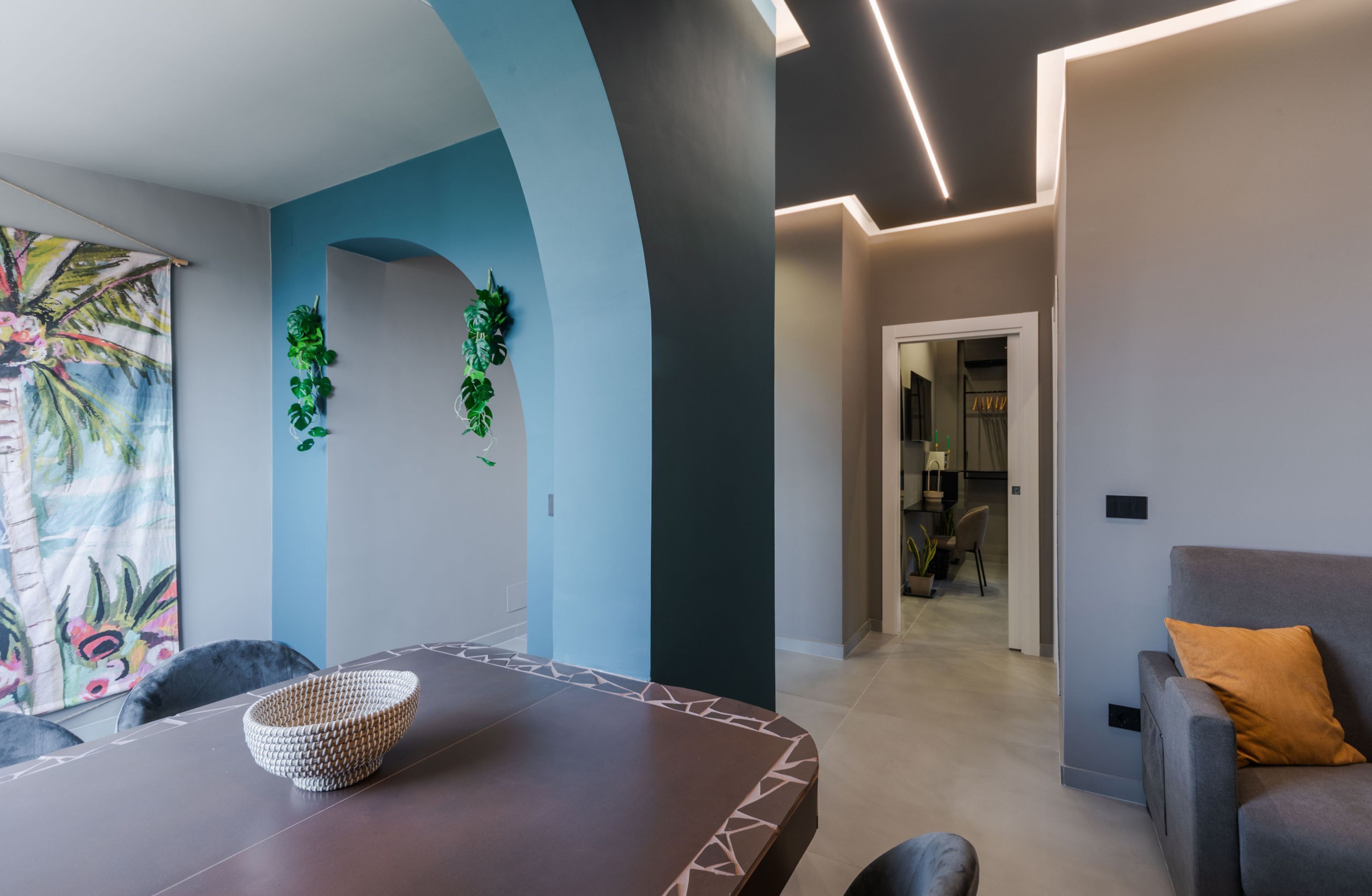 Un interior moderno con un área de comedor que presenta una mesa y sillas de madera oscura, un cuenco tejido decorativo y un cuadro abstracto colorido.