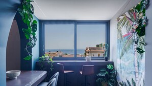 A modern room with a large window, a dining area with a table and chairs, and various potted plants. - Terrace Jacuzzi - Tropicalia by Wonderful Italy (Aci Castello)