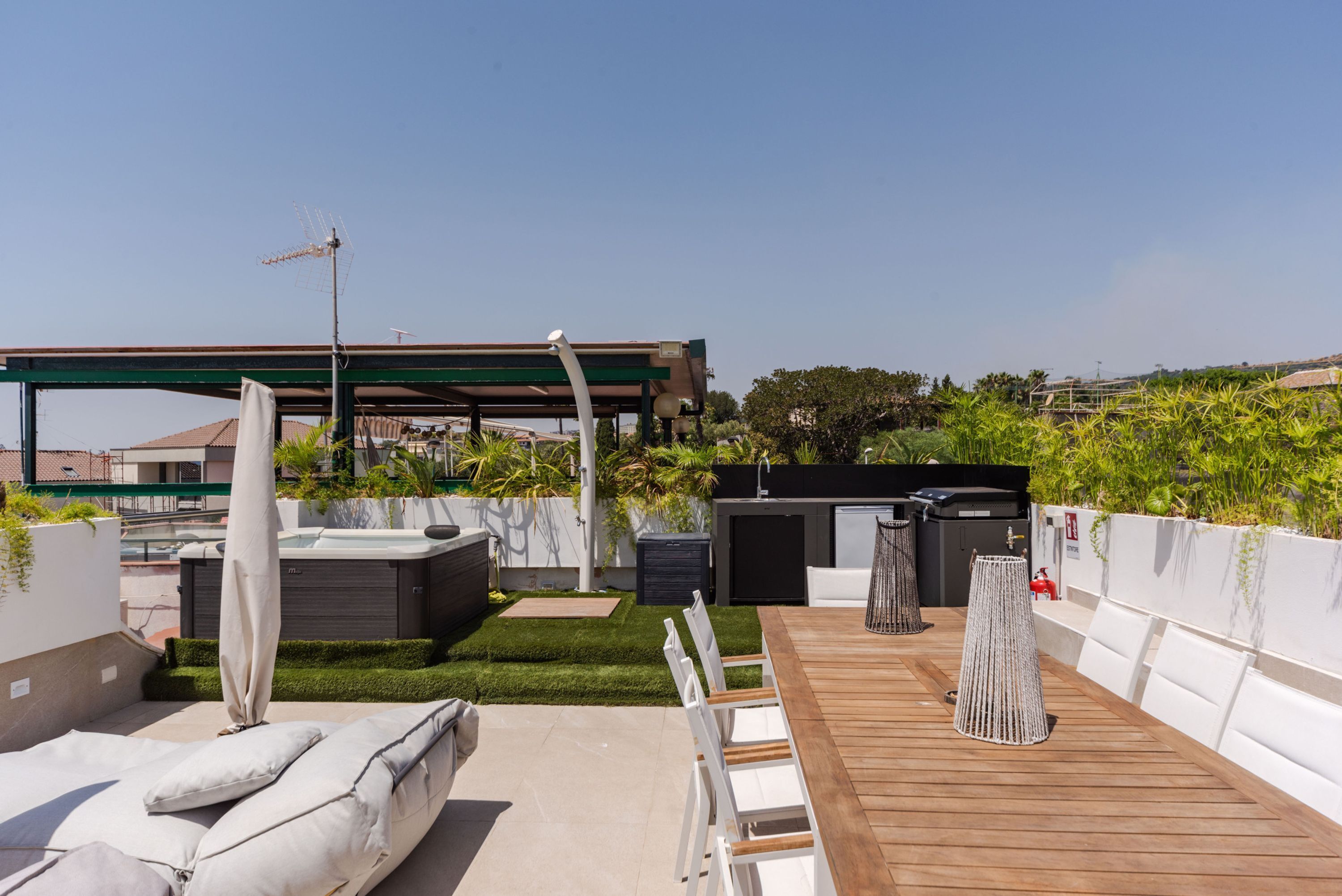 A rooftop patio with a wooden table and chairs, a hot tub, and a barbecue area.