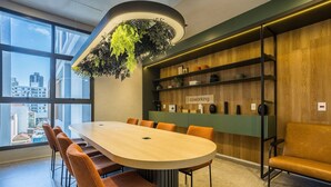 A modern meeting room with a long table, orange chairs, a green wall with shelves, and a hanging plant. - Full Studio 1km From Puc-sp Aby40002 (São Paulo)