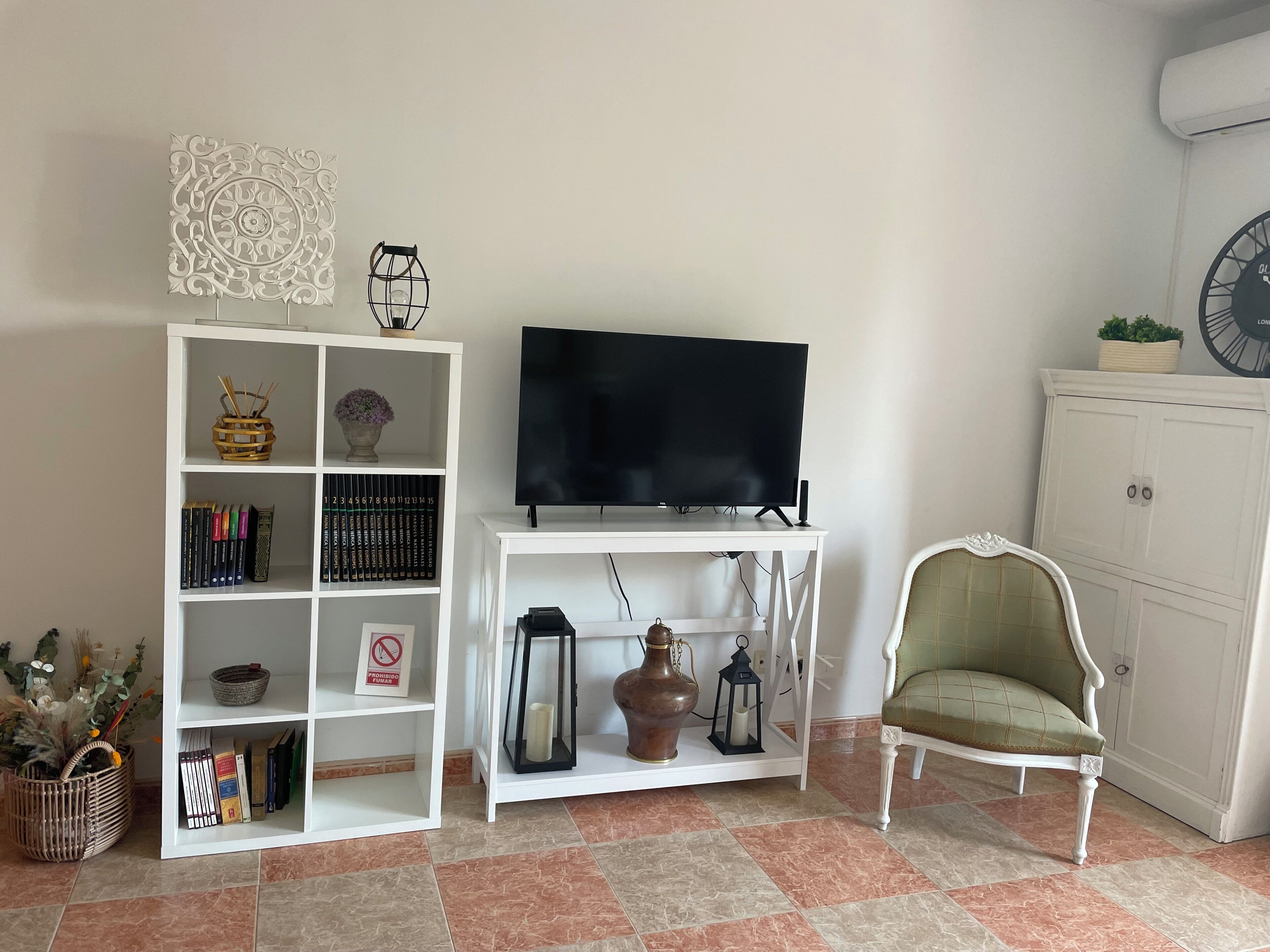 A living room with a white entertainment unit, a flat-screen TV, a green armchair, and a white cabinet.