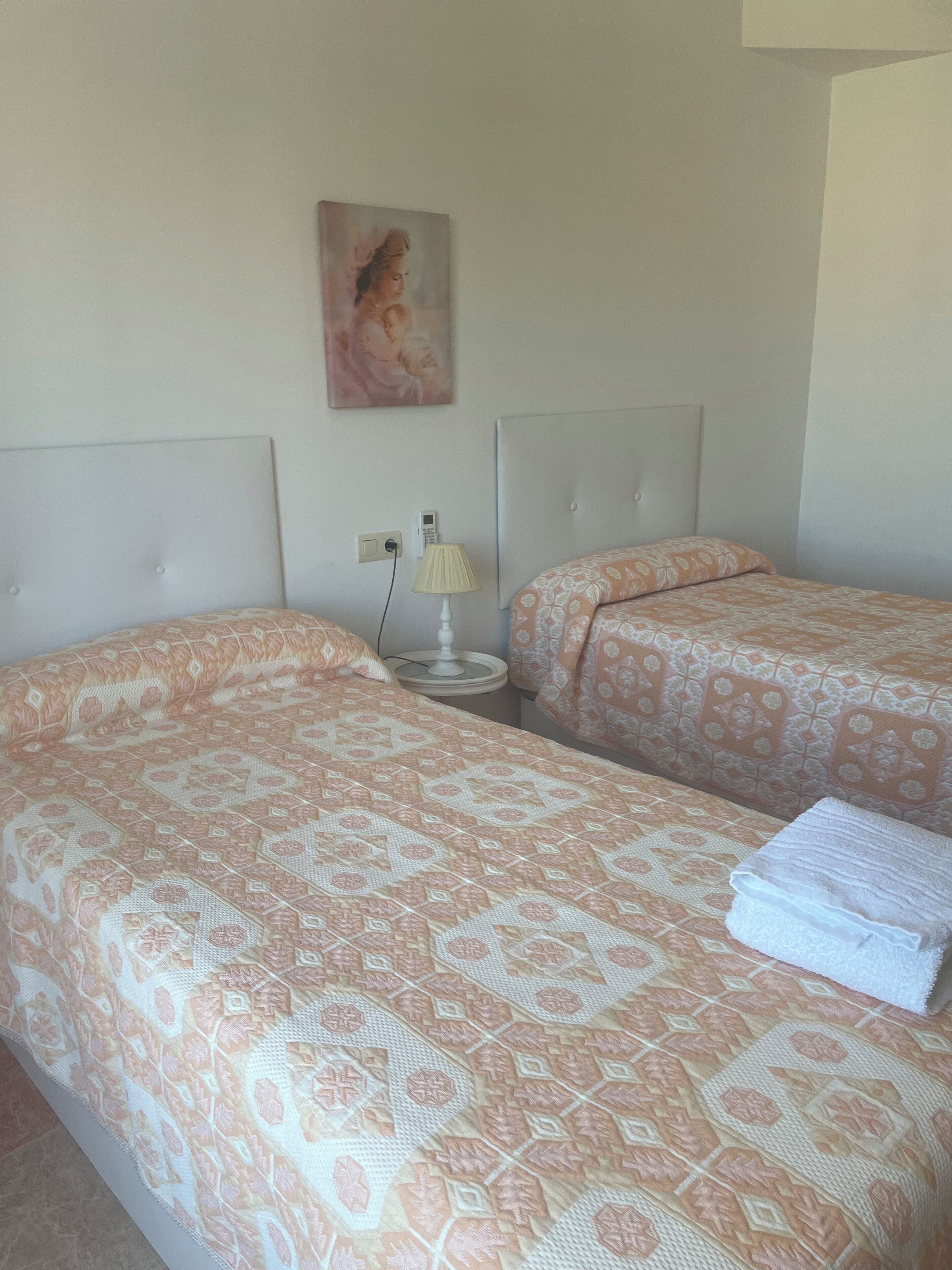 Habitación de hotel con dos camas, cada una con ropa de cama estampada, una mesita de noche con lámpara y un cuadro en la pared.