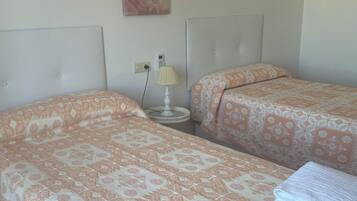 Habitación de hotel con dos camas, cada una con ropa de cama estampada, una mesita de noche con lámpara y un cuadro en la pared.