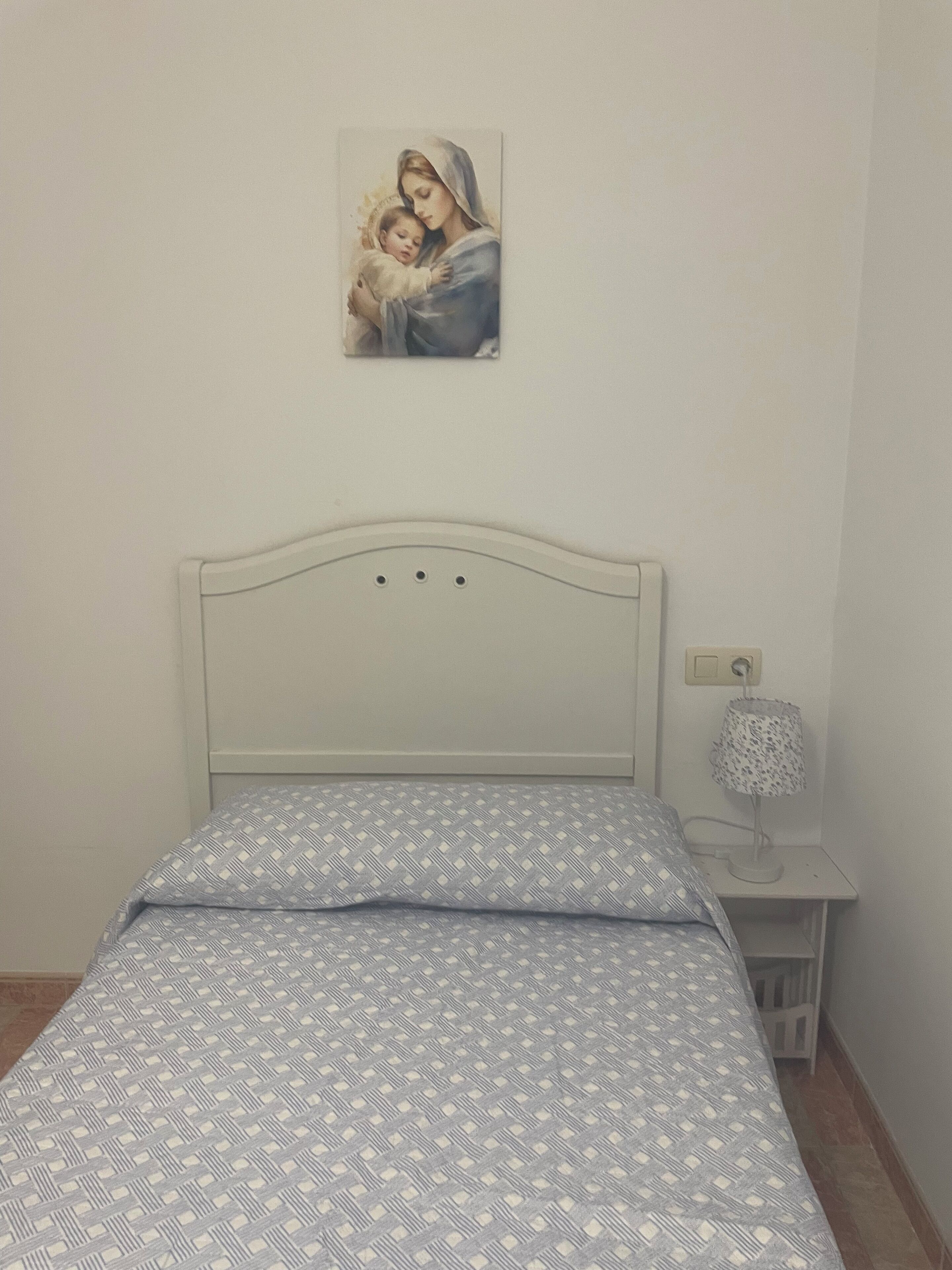 A bedroom with a bed, a nightstand, a lamp, and a wall-mounted picture.