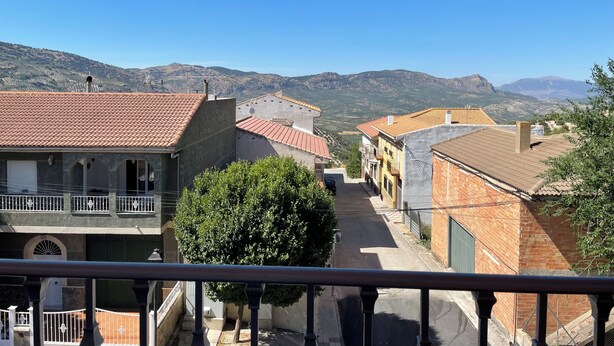 A narrow street with buildings on either side, a tree in the foreground, and mountains in the background. - El Mirador de Sierra Mágina II ( ideal for family travel) (Noalejo)
