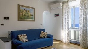 A blue sofa with floral cushions, a framed painting on the wall, and a window with curtains. - Quinto Easy Stay by Wonderful Italy (Genoa)