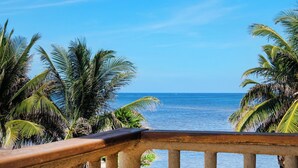 A view of the ocean from a balcony with a wooden railing, surrounded by palm trees. - 2BR Oceanfront Condo w/ Pools, Balcony + Views (San Pedro Town)