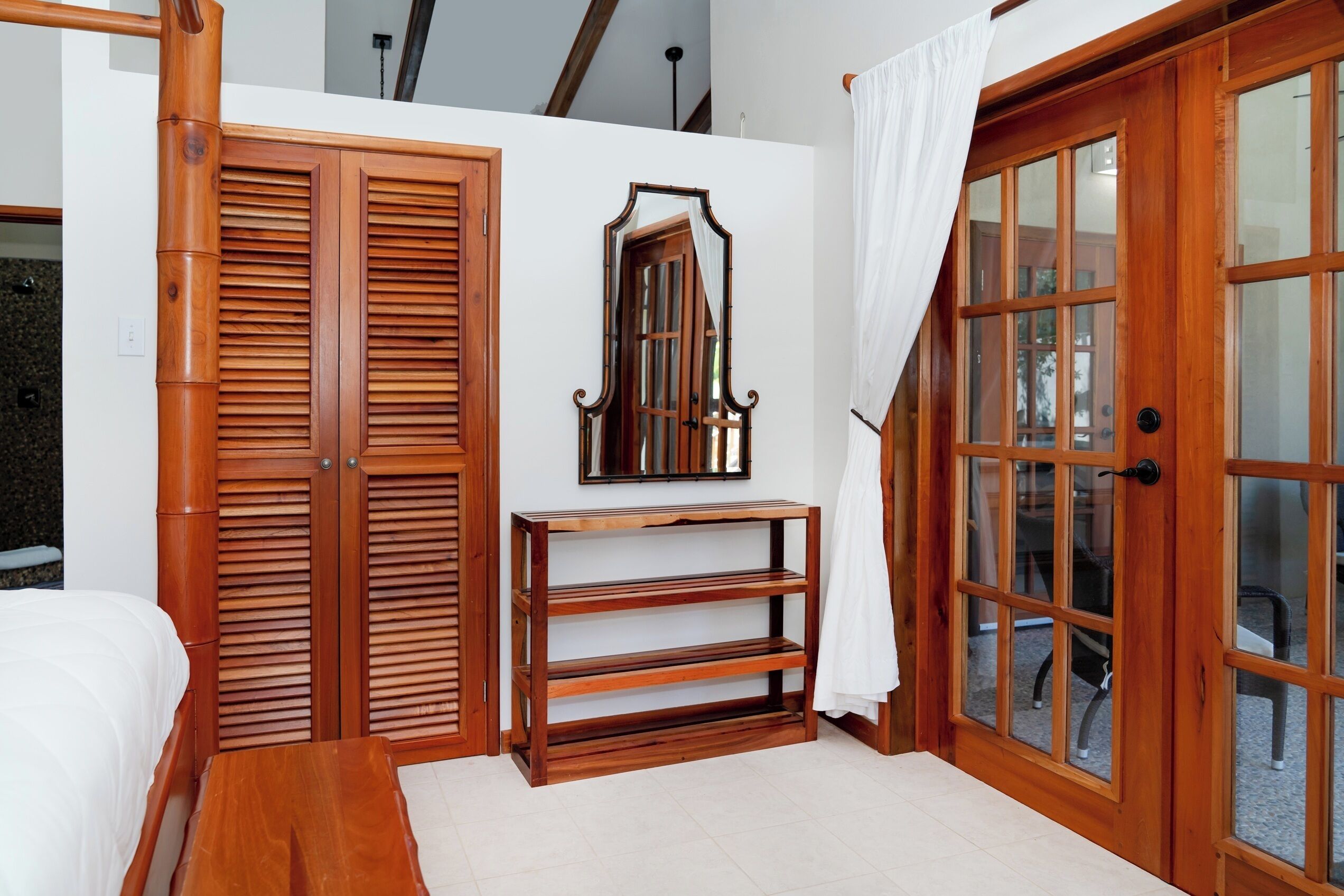 Una habitación con cama, armario de madera, un espejo y una puerta con paneles de vidrio.