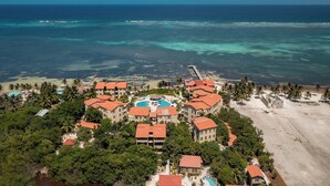 Vue aérienne d’un complexe hôtelier comprenant plusieurs bâtiments, une piscine centrale et une plage.