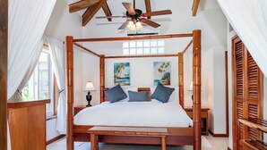Un lit à baldaquin avec une tête de lit en bois, un banc au pied du lit et un ventilateur de plafond au-dessus.