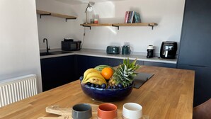 A kitchen with a wooden table, a fruit bowl, and three cups on a cutting board. - 6 Gwelfor Estate (Cemaes Bay)