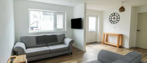 A modern living room with a grey sofa, a wooden coffee table, and a television mounted on the wall.