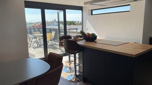 A modern kitchen with a wooden countertop, a dining area with a round table and chairs, and a view of the outdoors through large windows. - 6 Gwelfor Estate (Cemaes Bay)