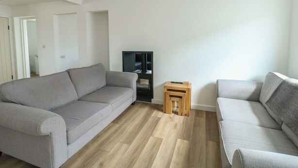 A modern living room with a grey sofa, a wooden coffee table, and a flat-screen TV. - 6 Gwelfor Estate (Cemaes Bay)