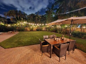 Un espacio al aire libre con patio, una mesa y sillas de madera, rodeado de piso de ladrillo y un césped cuidado.