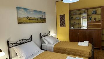 A hotel room with two beds, a painting of a landscape, a wooden cabinet with glass doors, and a hanging tapestry.