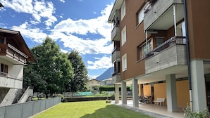 Un patio con un césped cuidado, una valla de madera y un edificio con balcones y un área cubierta.