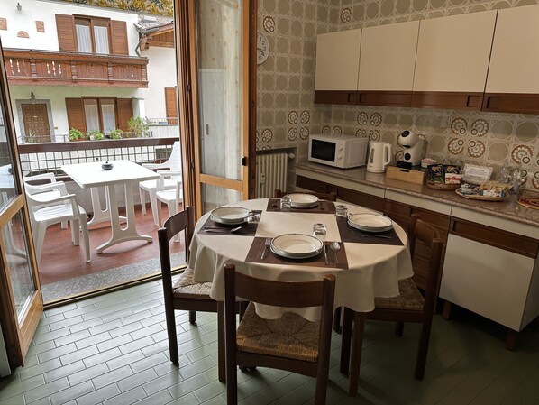A dining area with a table set for four, a kitchen with modern appliances, and a view of a building with balconies.