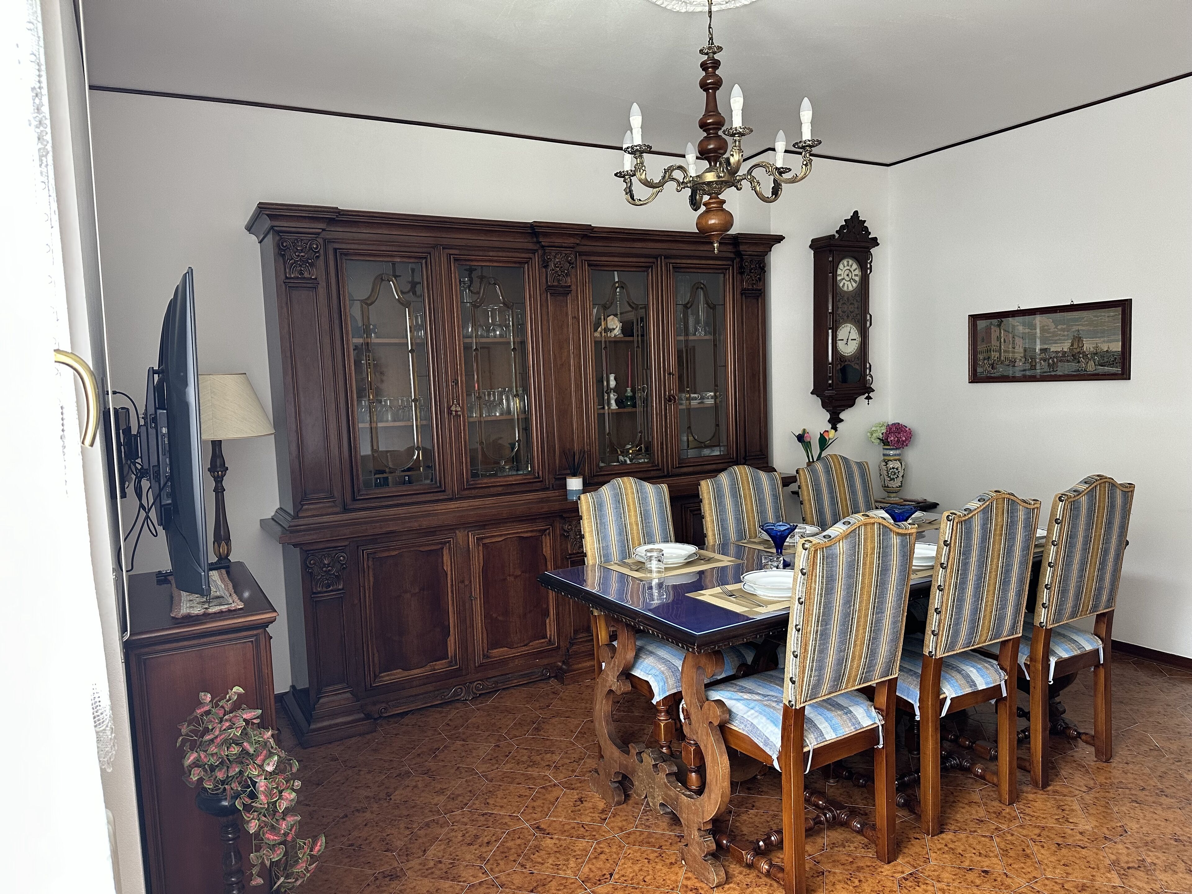 Ein Esszimmer mit Holztisch, gestreifte Stühle, einer Pendelleuchte, einer Vitrine und einer Wanduhr.