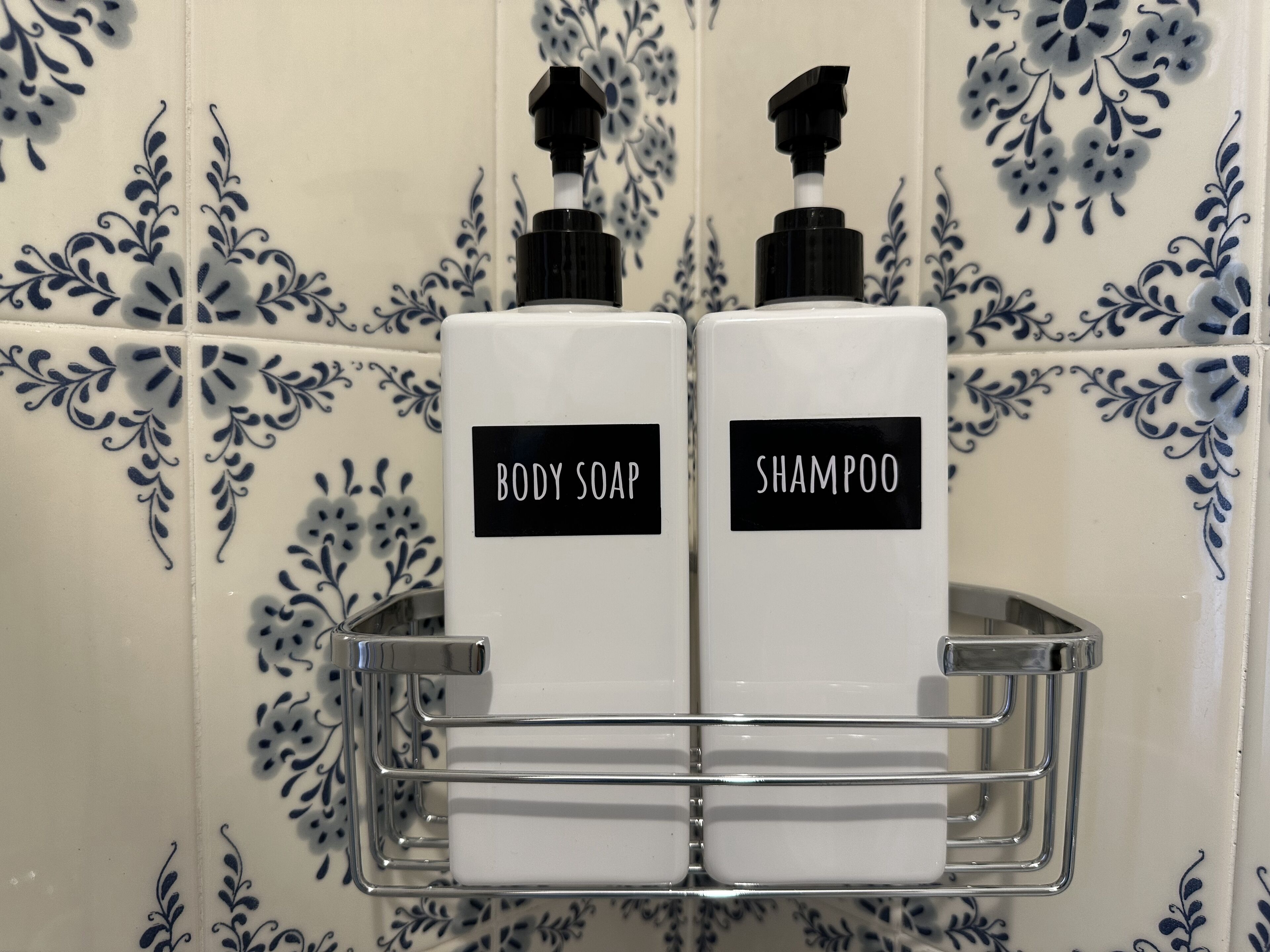 To flasker med sæbe og shampoo i et badeværelse med dekorative blå og hvide fliser.