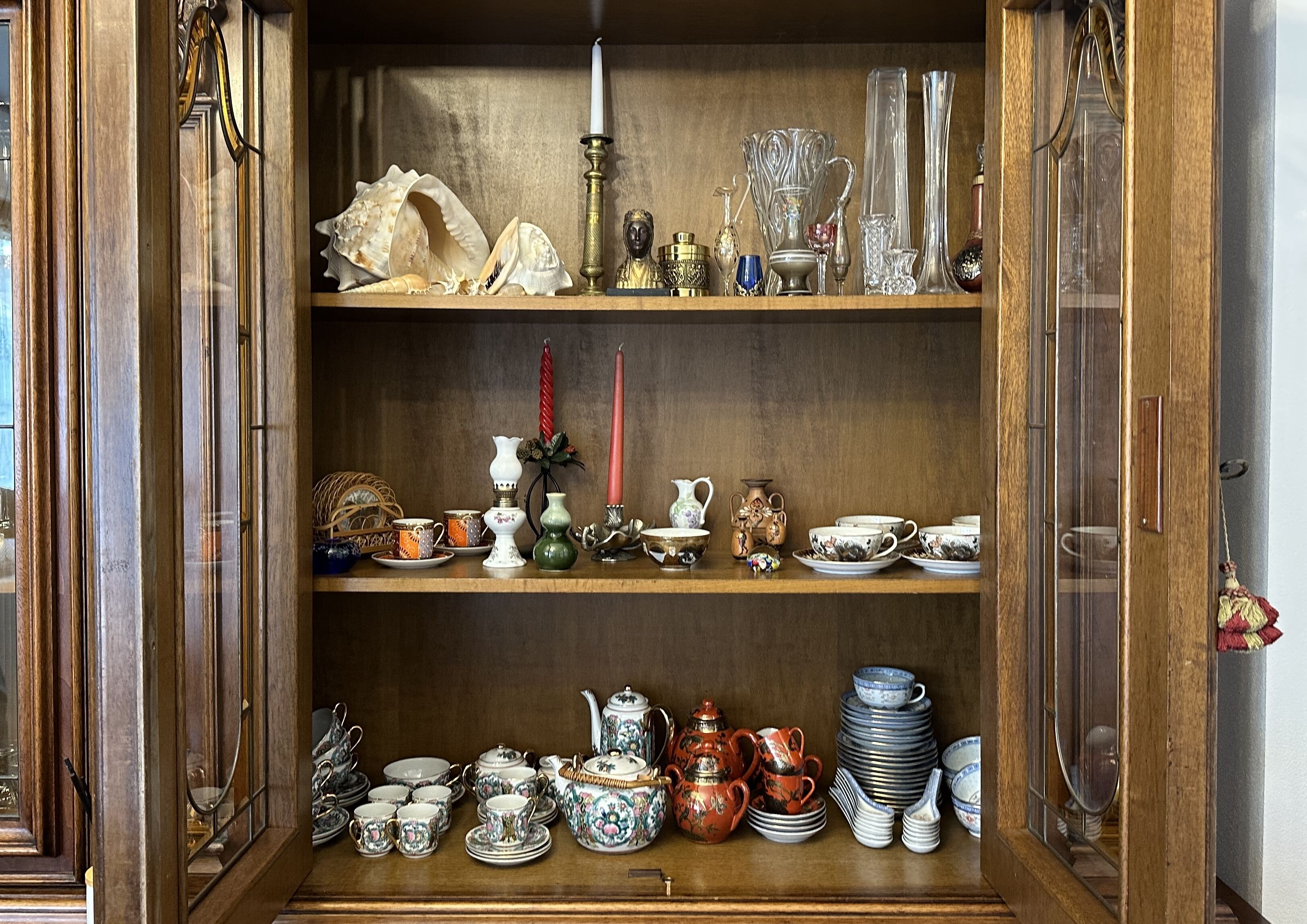 Un meuble en bois doté d’étagères où sont rangés divers objets en verre, en céramique et des couverts en argent.