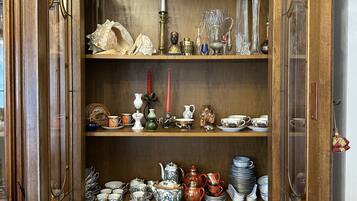 Un meuble en bois doté d’étagères où sont rangés divers objets en verre, en céramique et des couverts en argent.