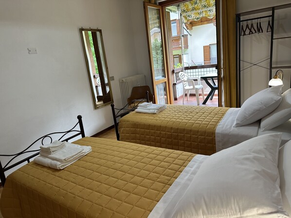 A hotel room with two beds, a window, a radiator, and a view of the outside balcony.