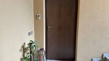 Una porta in legno con pomello, una piccola pianta in vaso e un boccale di metallo su uno scalino.