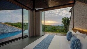 A bedroom with a large bed, a view of a stone wall and greenery, and a wooden deck outside. - 2bedrooms garden view villa unit 2 (Badung Regency, Bali)