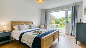 Una camera da letto con un letto di legno, un comodino, una cassettiera e vista sul giardino tramite una porta scorrevole in vetro.