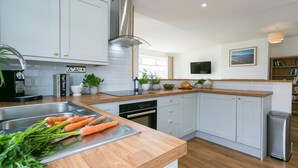 Una cucina moderna con mobili bianchi, un piano di lavoro in legno e un forno integrato. Si nota un lavello con un rubinetto, un piano cottura e una finestra sopra il lavello.