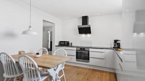 Een moderne keuken met witte kastjes, een houten eettafel en een zwarte afzuigkap.