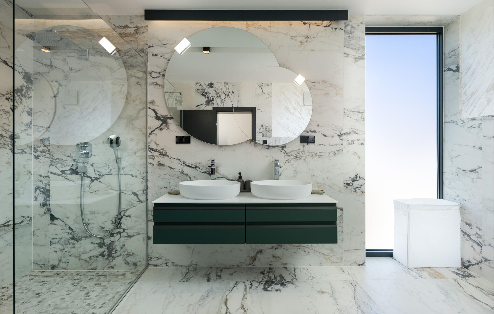 Un baño moderno con dos lavamanos grandes de color blanco, un mueble de tocador verde oscuro y un espejo amplio sobre los lavamanos.
