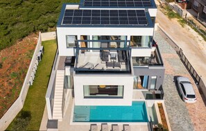 A modern multi-story house with a rooftop solar panel array, a swimming pool, and a car parked nearby. - Stunning home in Pula with sauna (Pula)